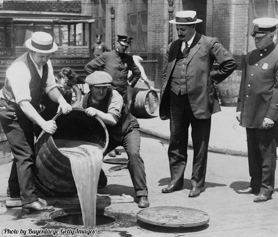 Agentes de Nova Iorque despejando álcool no esgoto após uma apreensão durante o auge da proibição, por volta de 1921