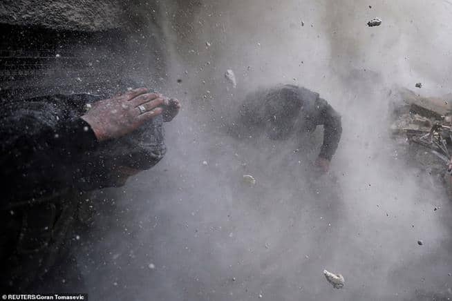 Rebeldes sírios esquivam-se dos escombros depois que um muro que usavam como barreira foi atingido por uma bala disparada por combatentes do governo, em Damasco, Síria, em 30 de janeiro de 2013