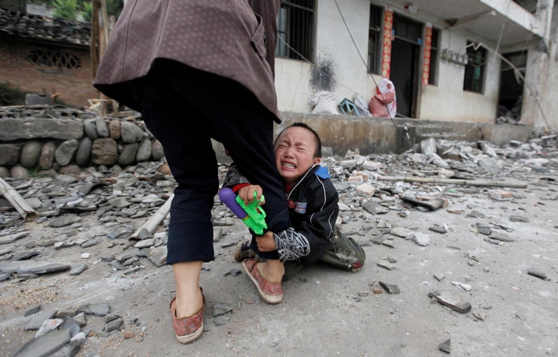 Menino se agarra à perna da mãe enquanto chora em frente a casa destruída após um terremoto de magnitude 6,6 na escala Richter, em Ya'an, China, 21 de abril de 2013