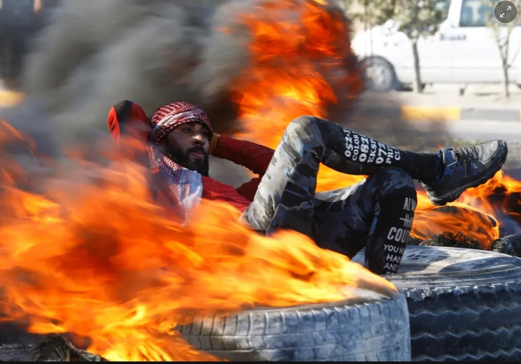 Manifestante iraquiano cercado por pneus em chamas durante protestos antigovernamentais