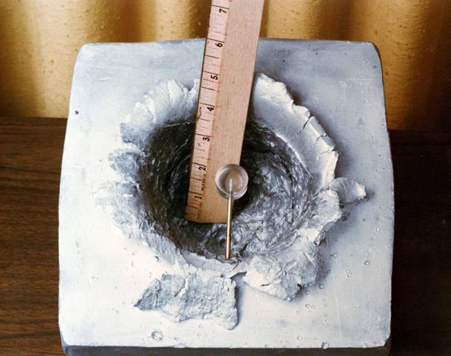 Cratera em um bloco de alumínio causada por uma moeda de um centavo disparada a uma velocidade orbital de 9 mil metros por segundo