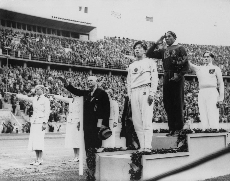 Jesse Owen (EUA) durante premiação após terminar em 1º lugar no salto em distância nos Jogos Olímpicos de Verão de 1936, realizados em Berlim, com Luz Long (Alemanha) em 2º e Naoto Tajima (Japão) em 3º lugar.