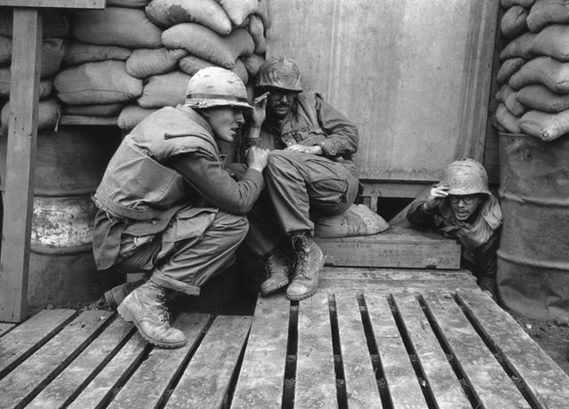 Três fuzileiros navais americanos protegem-se enquanto foguetes norte-vietnamitas caem na base norte-americana em Khe Sanh, sul do Vietnã, em 12 de fevereiro de 1968.