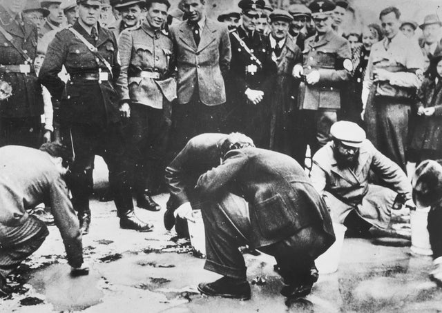 Judeus sendo forçados a esfregar o chão das ruas de Viena enquanto são observados por nazistas austríacos e residentes locais, em 1938.