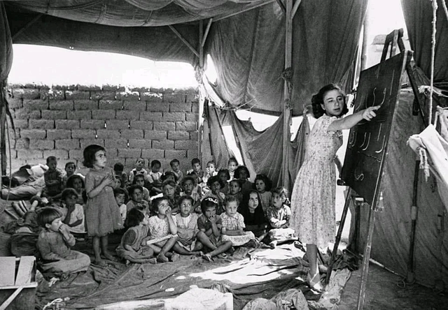 Uma professora palestina e seus alunos dentro de uma barraca que foi usada como sala de aula improvisada em um campo de refugiados palestinos perto da cidade de Zarqa, na Jordânia, 1949