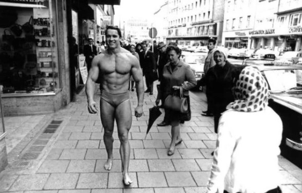 Arnold Schwarzenegger caminhando por uma rua de Munique de sunga para promover sua própria academia, 1969.