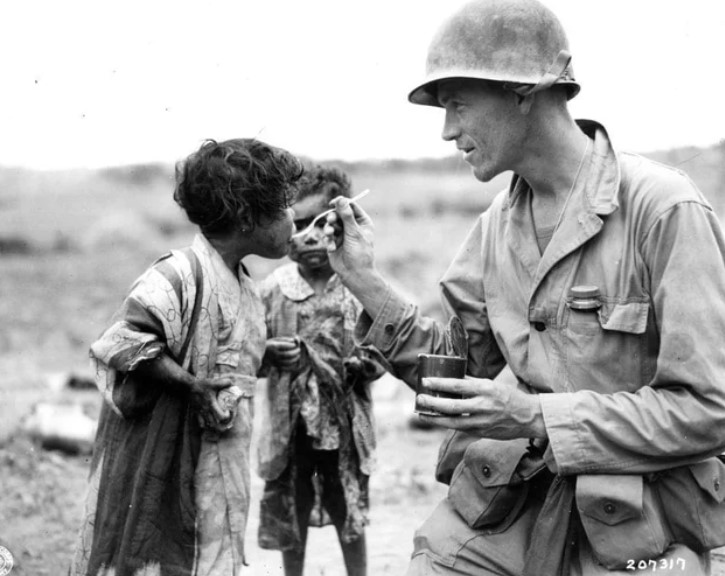 O tenente Richard Jones, de Los Angeles, alimentando duas crianças japonesas que estavam escondidas em uma tumba abandonada, a 50 metros da linha de frente durante a batalha de Okinawa, em 31 de maio de 1945. Ele sobreviveu à guerra e faleceu em 23 de março de 2004, aos 89 anos.