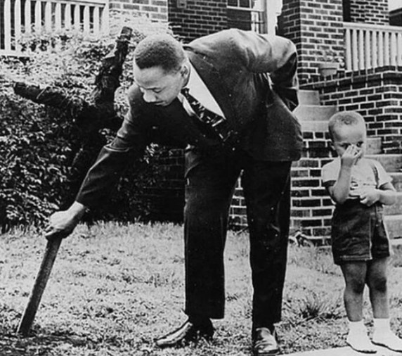 Martin Luther King Jr removendo uma cruz queimada de seu jardim, em 1960.