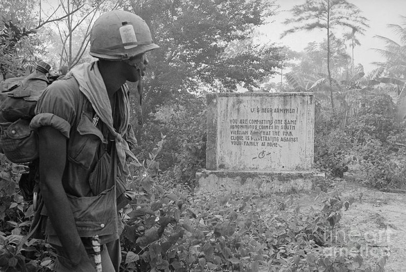 Soldado negro dos EUA lê uma mensagem deixada pelos Viet Côngs durante a Guerra do Vietnã. A mensagem diz: 