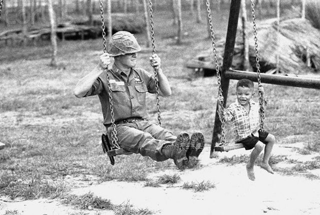 Soldado norte-americano e uma criança vietnamita se balançando em acampamento base de Cu Chi, Vietnã do Sul (1966).