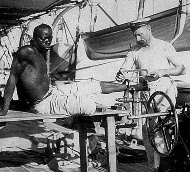 Algemas de um homem escravisado sendo cortada por um ferreiro depois que a escravidão foi proibida na maior parte do mundo. A pessoa foi resgatada na costa de Omã, 1907.