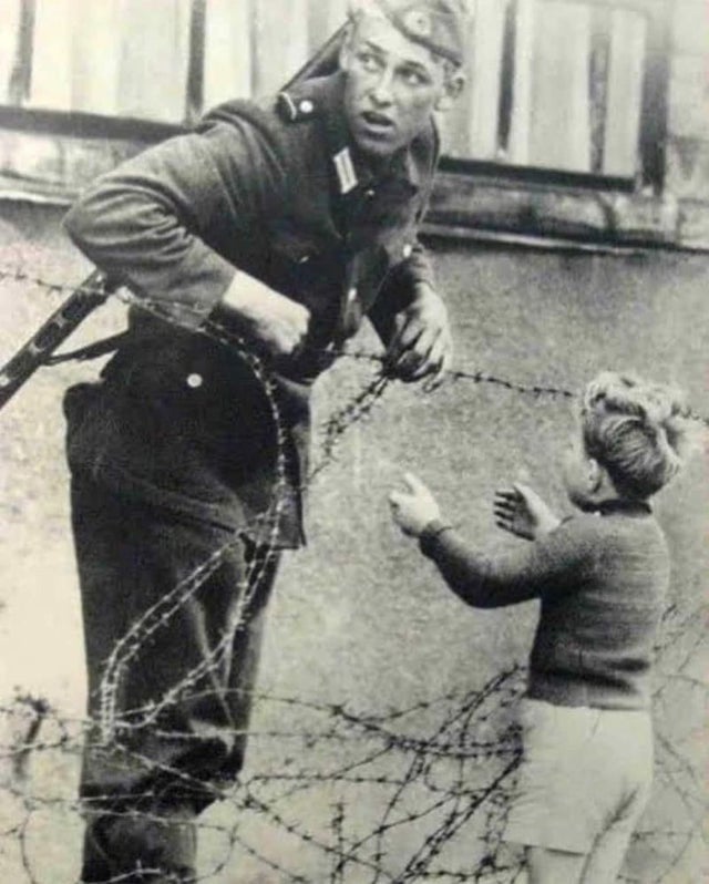 Foto icônica de um soldado da Alemanha Oriental ajudando um menino a atravessar o Muro de Berlim no dia em que foi erguido, em 1961. O menino foi deixado para trás durante o caos de pessoas fugindo.