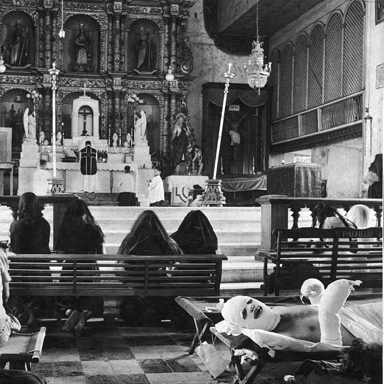 Oficial americano gravemente queimado deitado em uma maca de hospital em uma igreja em Layte, enquanto acontecia uma missa. A igreja funcionou como hospital temporário. Filipinas, 1944.
