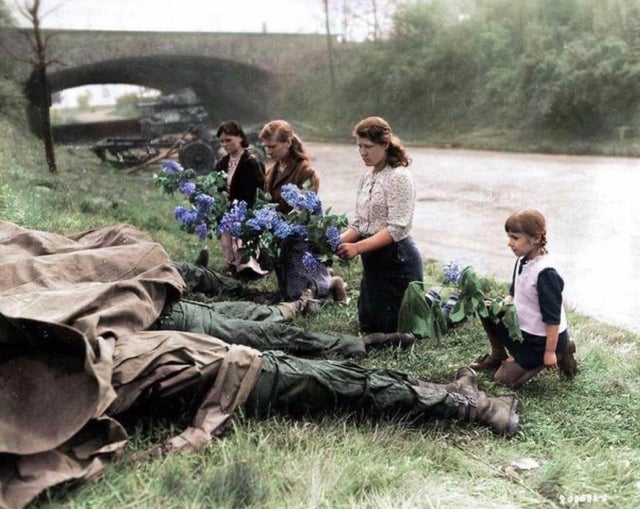 Mulheres russas libertadas de um campo de trabalho escravo depositam flores aos pés de soldados americanos mortos - 1944.